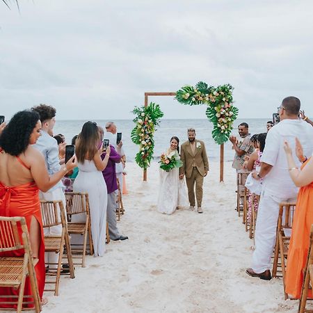 Impressive Punta Cana Esterno foto The photo depicts a wedding ceremony on a beach. In the center, there is an altar decorated with greenery and flowers. A couple is walking down the aisle, with guests on either side capturing the moment on their phones. The attendees are dressed in a