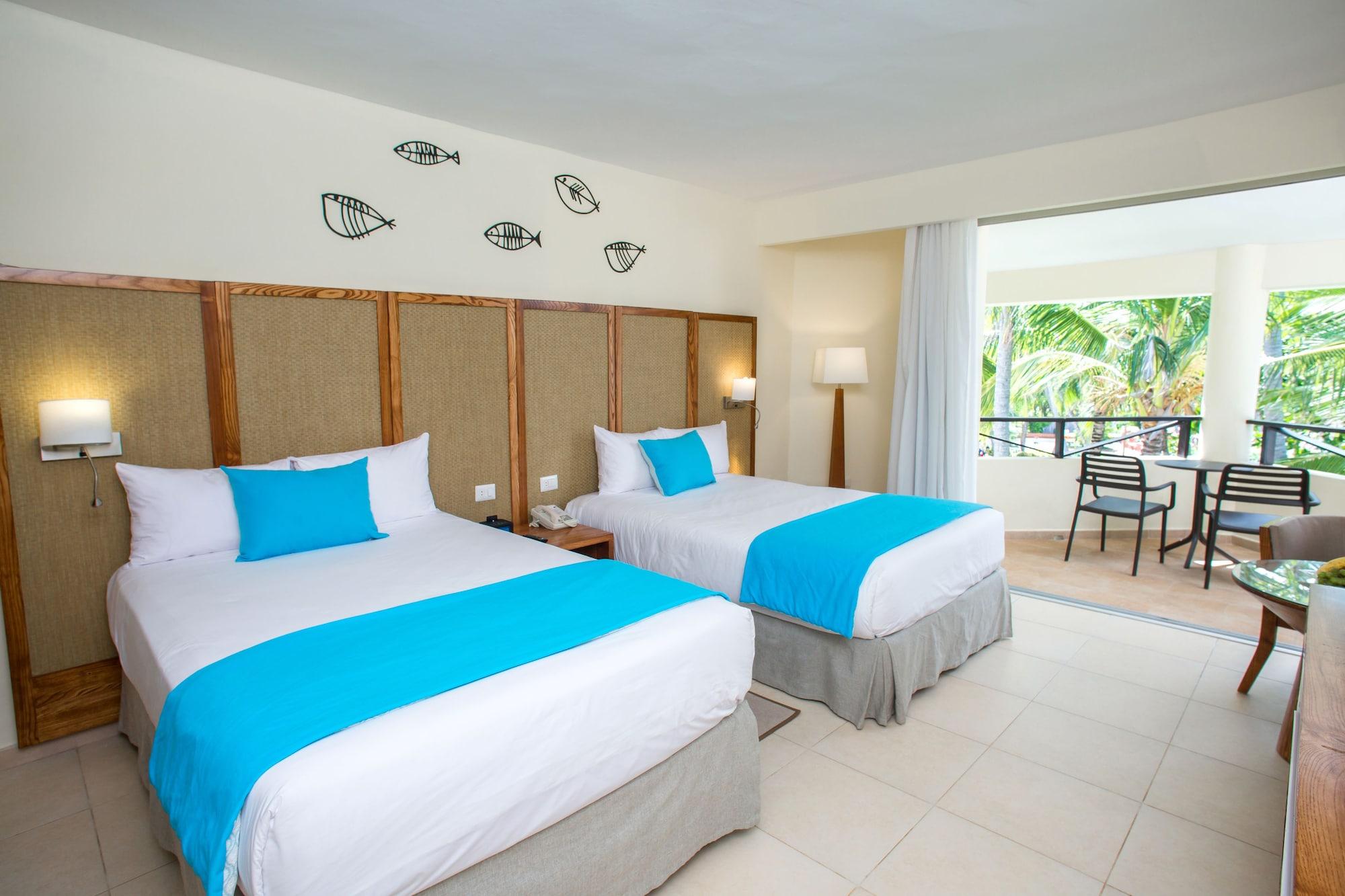 Impressive Punta Cana Esterno foto The photo shows a hotel room featuring two beds with white linens and bright turquoise decorative elements. The walls are light-colored, and there's a decorative pattern of fish above the beds. The room has a lamp beside one of the beds and a spaciou