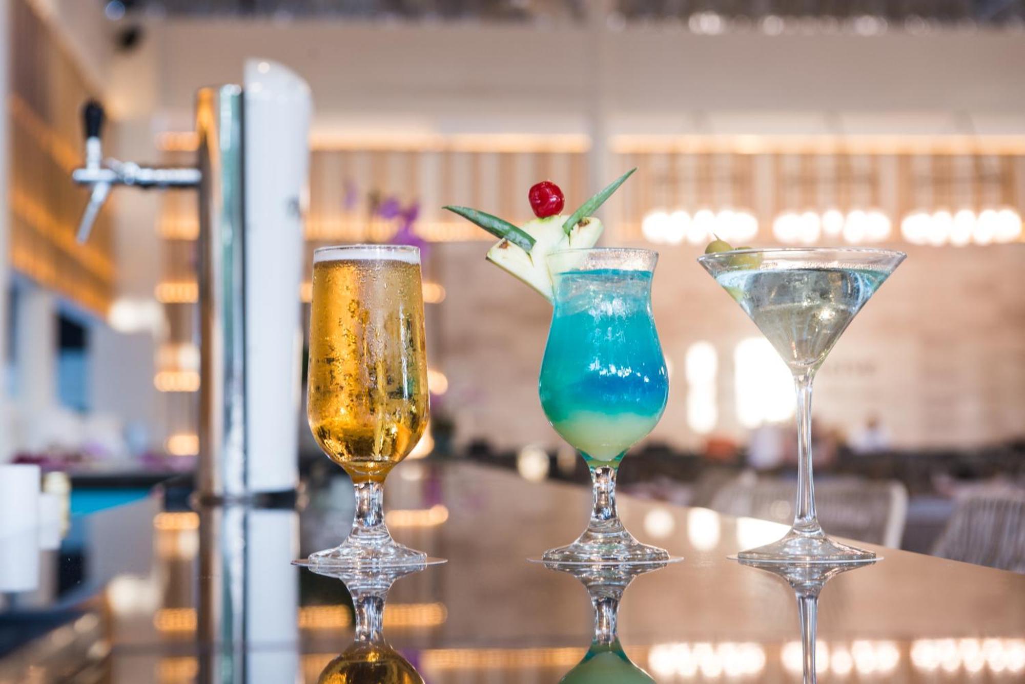 Impressive Punta Cana Esterno foto The photo features three different cocktails presented on a shiny surface. 

1. On the left, there is a tall glass of beer, which appears golden and bubbly, served in a flute-style glass.
2. In the center, a vibrant blue cocktail garnished with a pin