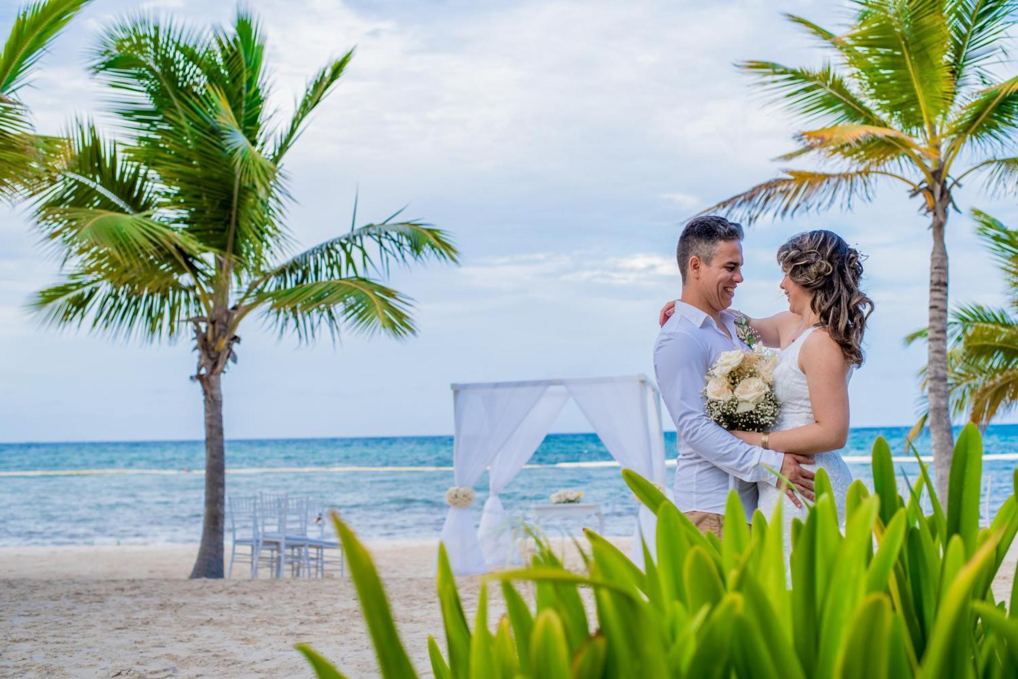 Impressive Punta Cana Esterno foto The photo depicts a couple embracing on a beach. They appear to be celebrating their wedding, as evidenced by the woman's bouquet. The scenic background features palm trees and the ocean, creating a romantic atmosphere. A white wedding canopy is set 